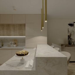 Design Atelier by Maria Słodowska - Beżowa kuchnia z marmurowym blatem i złotymi lampami wiszącymi. Na blacie ciasto. W tle obraz na ścianie i klimatyzator. Minimalistyczny styl.