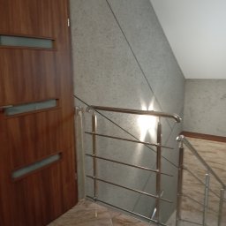 Efekt - Klatka schodowa po remoncie: brązowe drzwi z przeszkleniami, szara ściana z fakturą, metalowa barierka schodów i marmurowe płytki podłogowe.