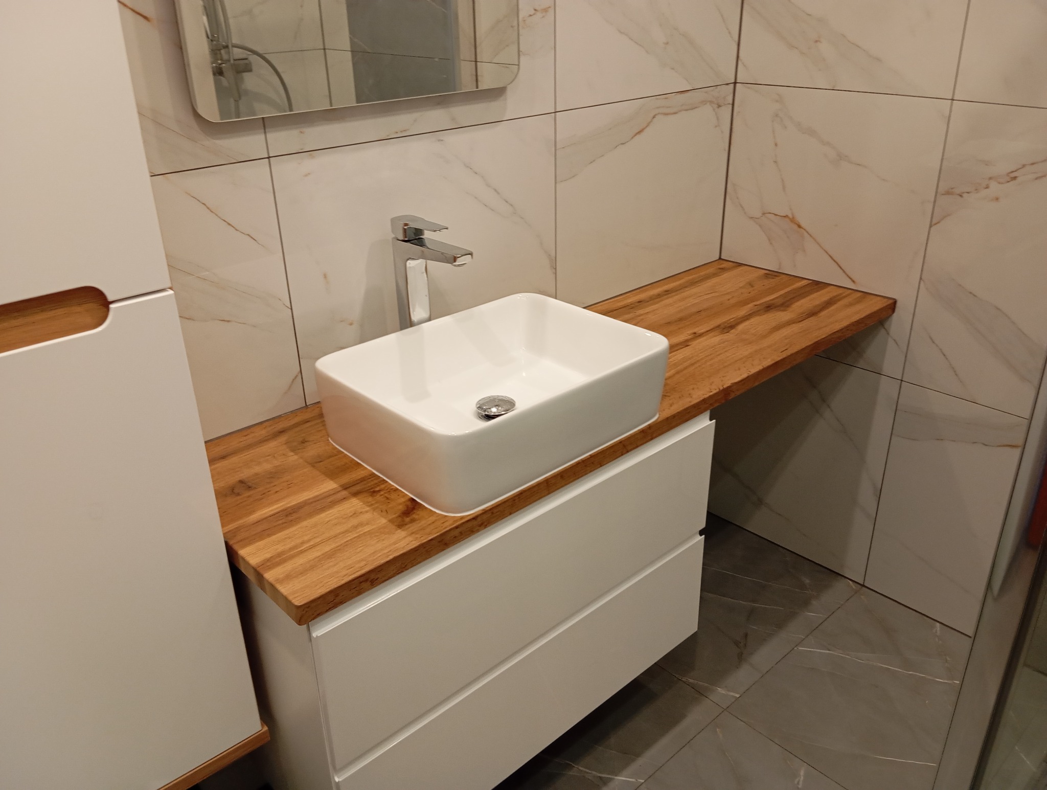 Nowoczesna łazienka: biała umywalka nablatowa na drewnianym blacie, minimalistyczna bateria, marmurowe płytki i białe szafki. Eleganckie wykończenie.