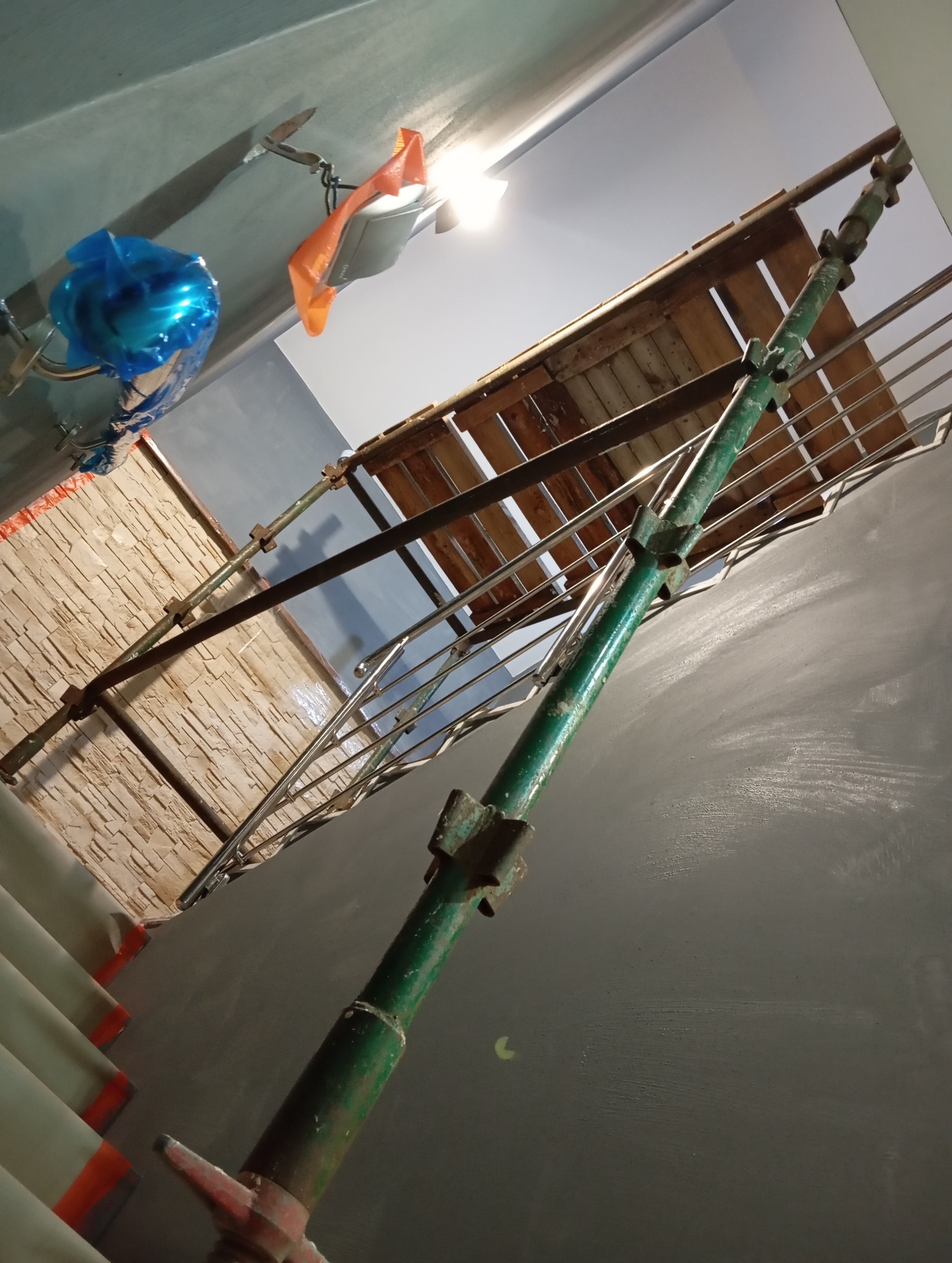 Ściana po szpachlowaniu/malowaniu z widocznymi rusztowaniami i lampą. Ujęcie z dołu ukazuje strukturę ściany i etap prac wykończeniowych.