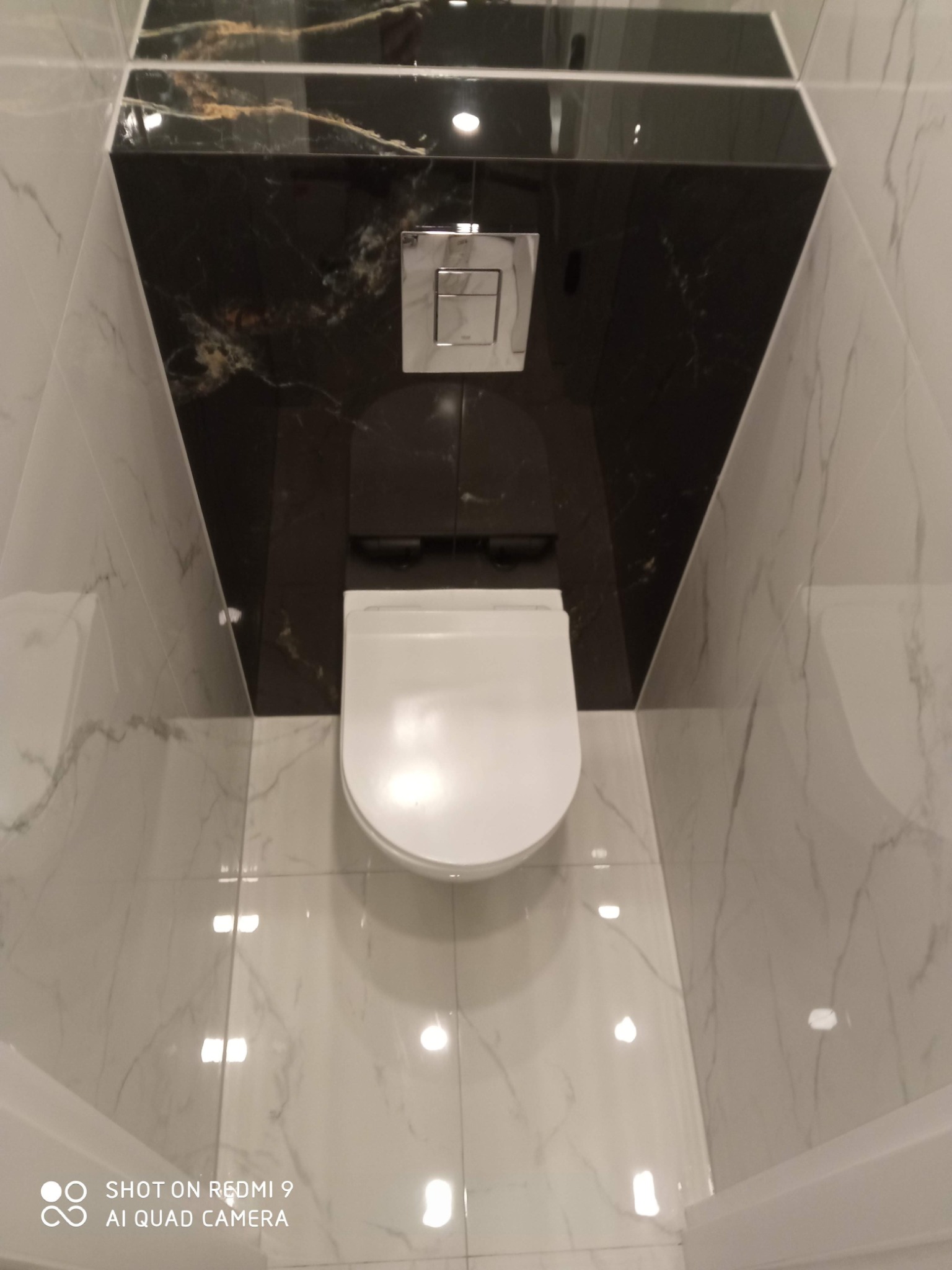 Nowoczesna toaleta podwieszana z czarnym marmurem w Stargardzie. Eleganckie wykończenie łazienki z białymi płytkami imitującymi marmur na podłodze i ścianach.