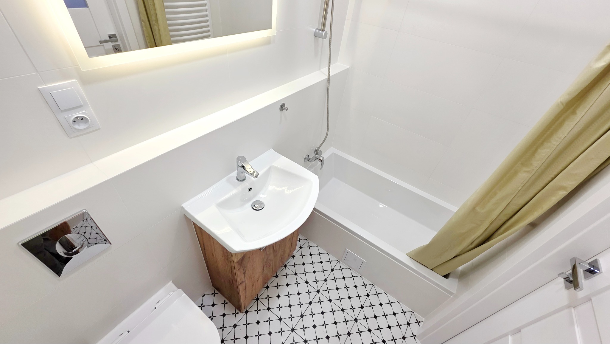 Biała łazienka po remoncie z kabiną prysznicową, umywalką z drewnianą szafką i czarno-białą podłogą w geometryczny wzór, widziana z góry.