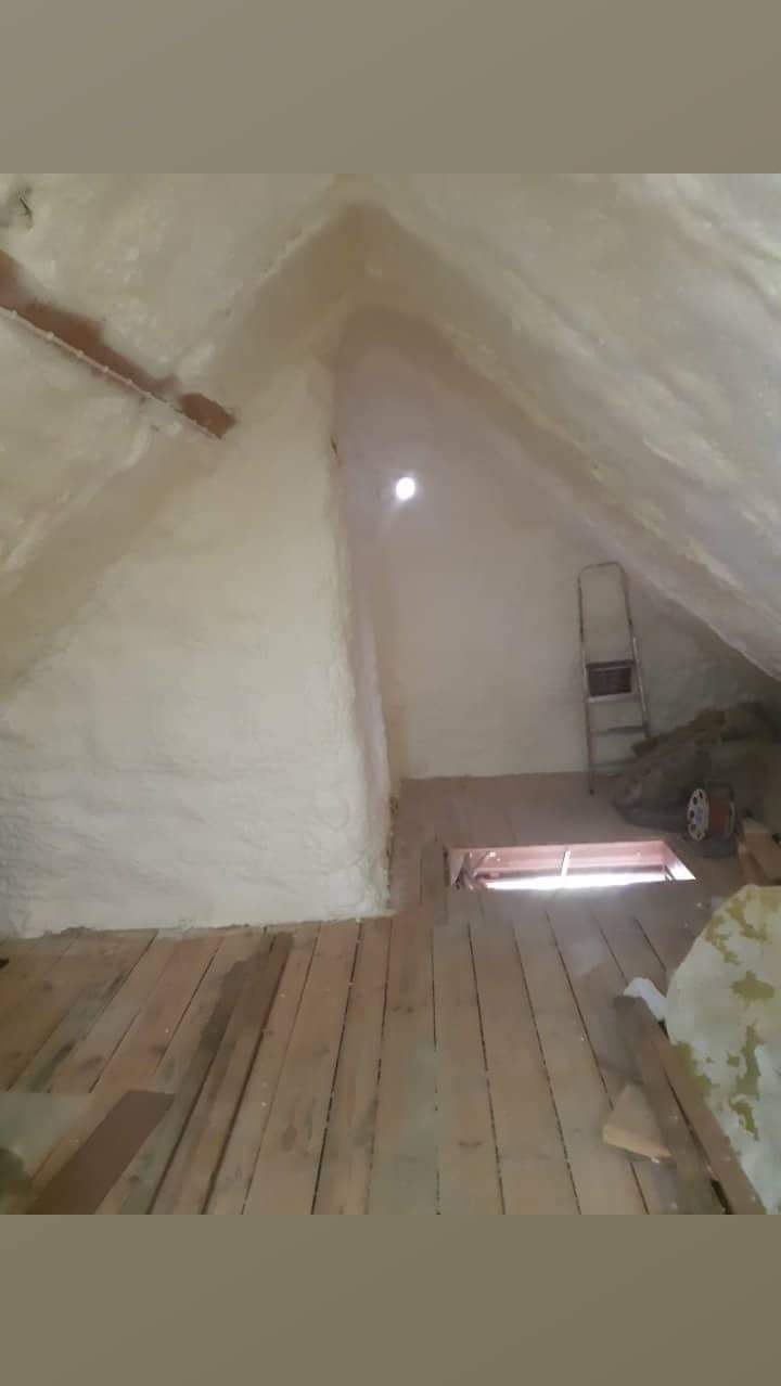 Poddasze po ociepleniu pianką PUR: biała izolacja na skośnych ścianach i suficie, drewniana podłoga, drabina oparta o ścianę. Widoczne detale struktury pianki.