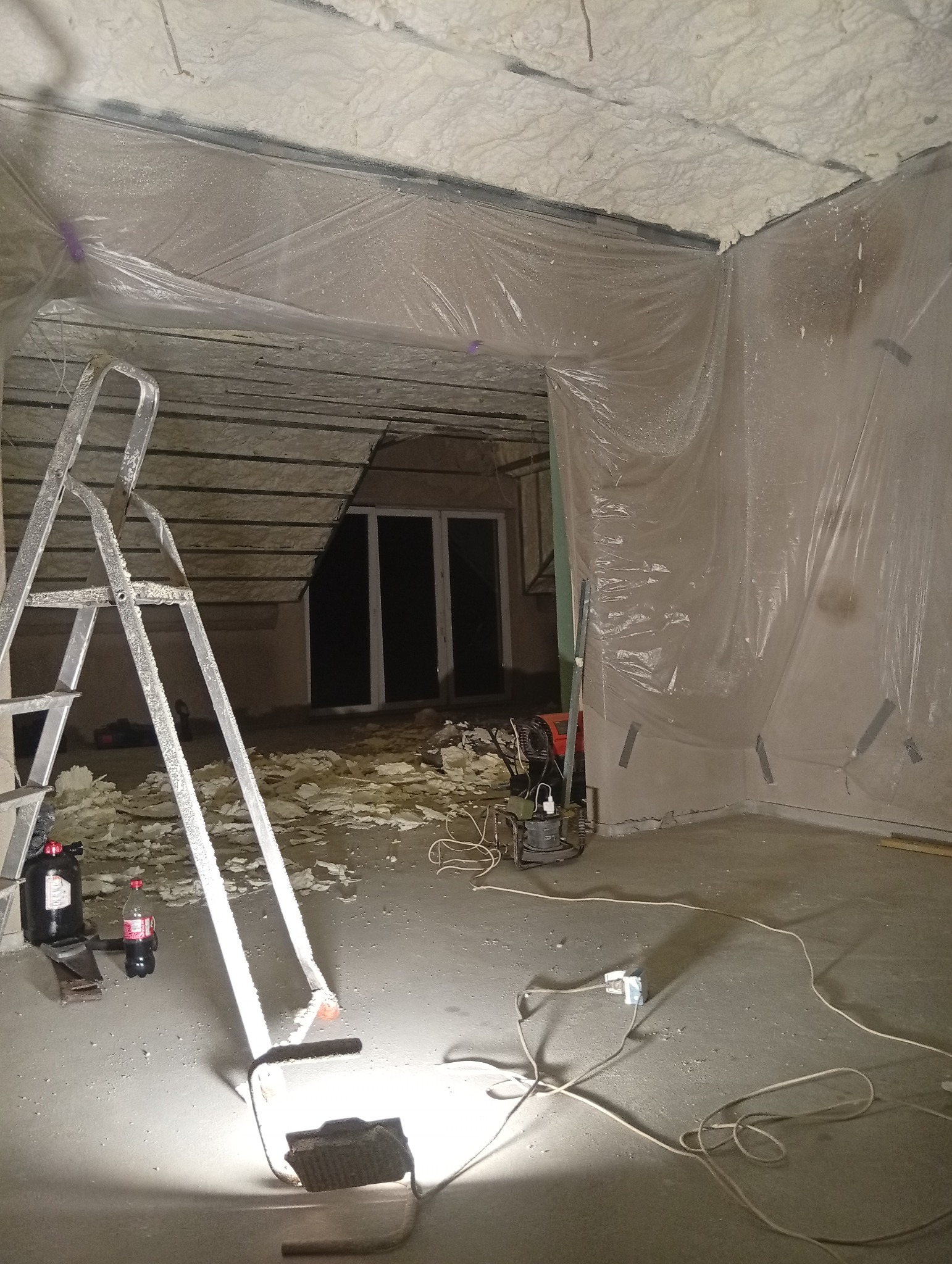 Poddasze w trakcie ocieplania pianką PUR, widoczne narzędzia, drabina i folia ochronna. Świeżo nałożona pianka na suficie i skosach.