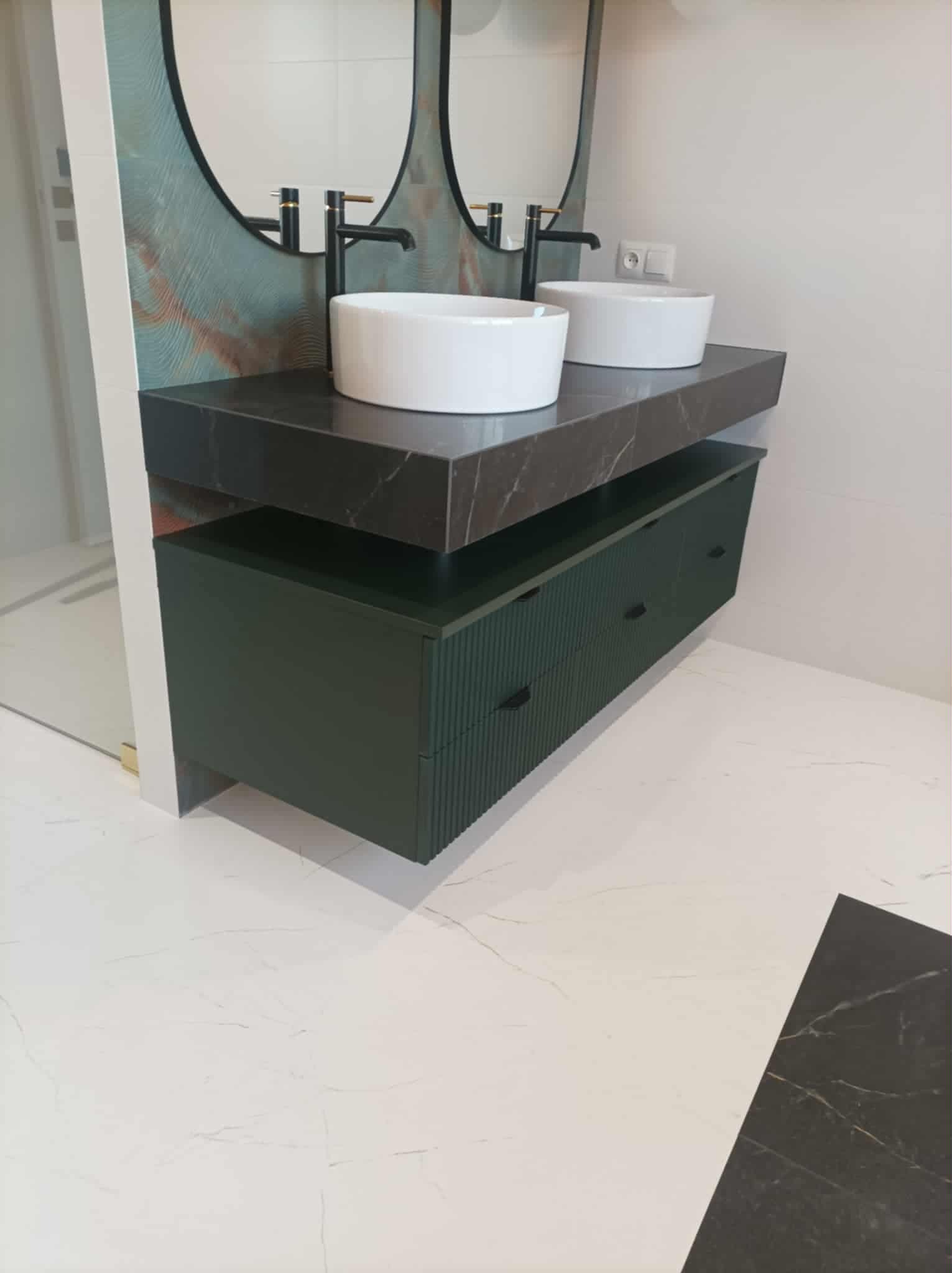 Nowoczesna szafka łazienkowa w odcieniach zieleni z marmurowym blatem i dwiema białymi umywalkami nablatowymi. Nad nią owalne lustra z czarną armaturą.