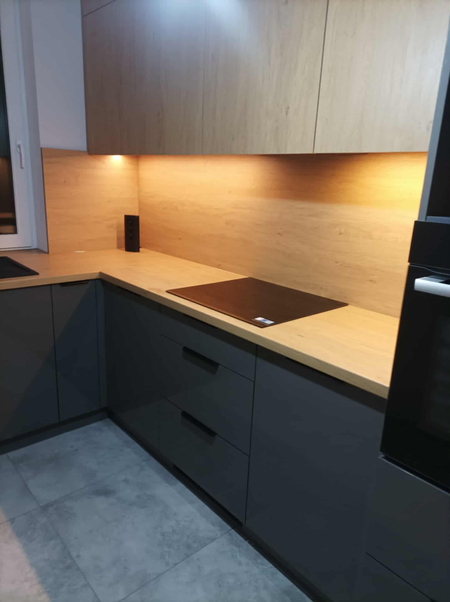 Nowoczesna kuchnia na wymiar w Kłomnicach: szare szafki z drewnianym blatem i płytą indukcyjną, oświetlenie podszafkowe, minimalistyczny design.