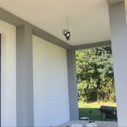 Świeżo pomalowana elewacja domu z szarymi akcentami, widok z zewnątrz na ogród. Na podłodze widoczne puszki z farbą, co sugeruje ukończone prace malarskie.