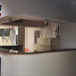 Jasne wnętrze biura z recepcją, wiszącymi lampami i pomarańczowymi krzesłami. Widoczny znak firmy na ścianie i drzwi w tle. Ściany pomalowane na biało.