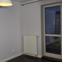 PLZ Painting And Decorating LTD - Pomalowane na szaro wnętrze pokoju z ciemną podłogą, białym grzejnikiem i lampą. Widoczne okno z zasłoną. Świeżo odnowione ściany.