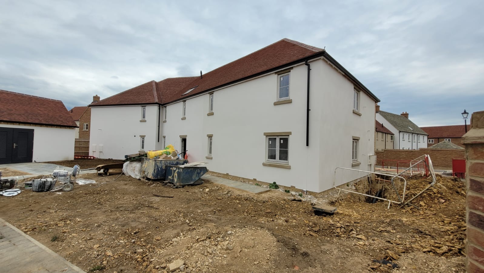 Biała elewacja budynku wielorodzinnego z czerwonym dachem po malowaniu, widoczne ślady prac wykończeniowych i pojemniki na odpady budowlane.