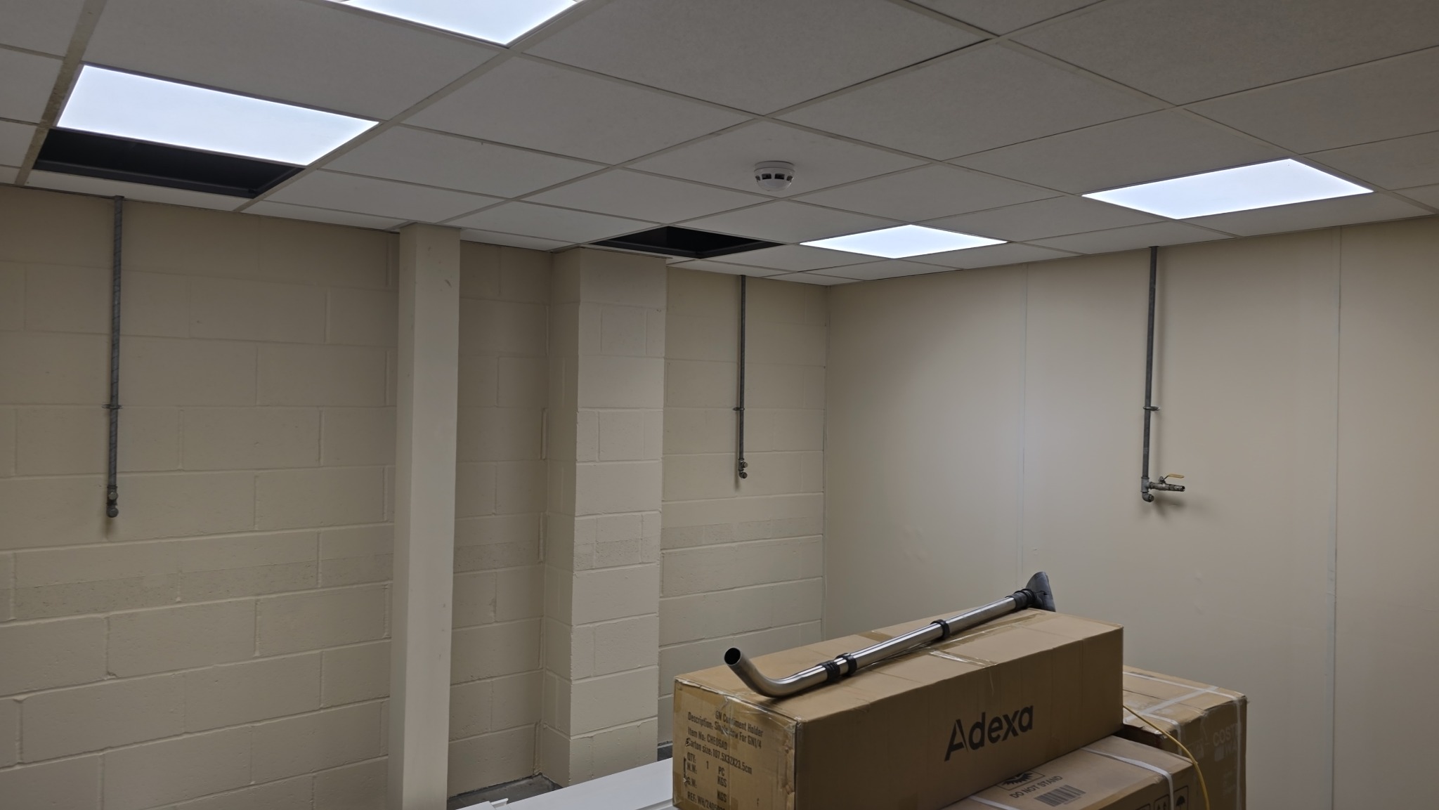 Wnętrze biura przed malowaniem: ściany z cegły i płyty, rury, kartony Adexa. Sufit kasetonowy z brakującymi panelami. Przygotowanie do prac wykończeniowych.