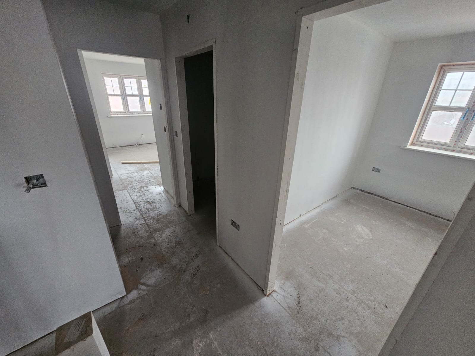 Wnętrze w trakcie prac wykończeniowych: świeżo pomalowane ściany na biało, widoczne otwory drzwiowe i okno. Na podłodze widoczny szary beton.