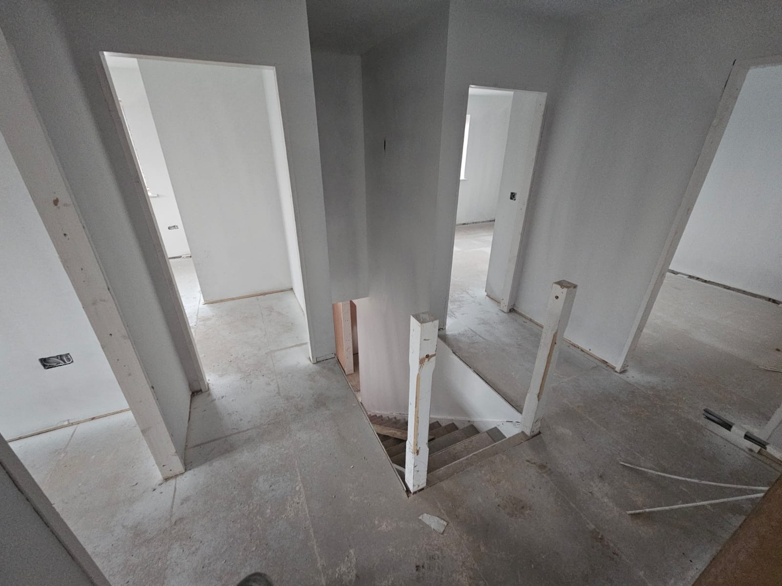 Wnętrze w trakcie malowania: białe ściany, widoczne przejścia między pomieszczeniami i schody. Surowy stan wykończenia, przygotowanie do dalszych prac.