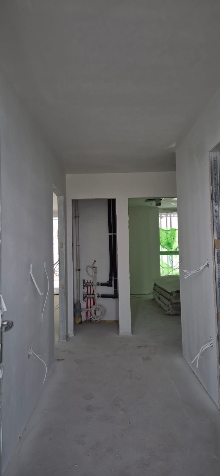 Wnętrze w trakcie malowania: świeżo pomalowane ściany w odcieniach szarości, widoczne instalacje oraz materiały budowlane. Minimalistyczny styl, surowe wykończenie.