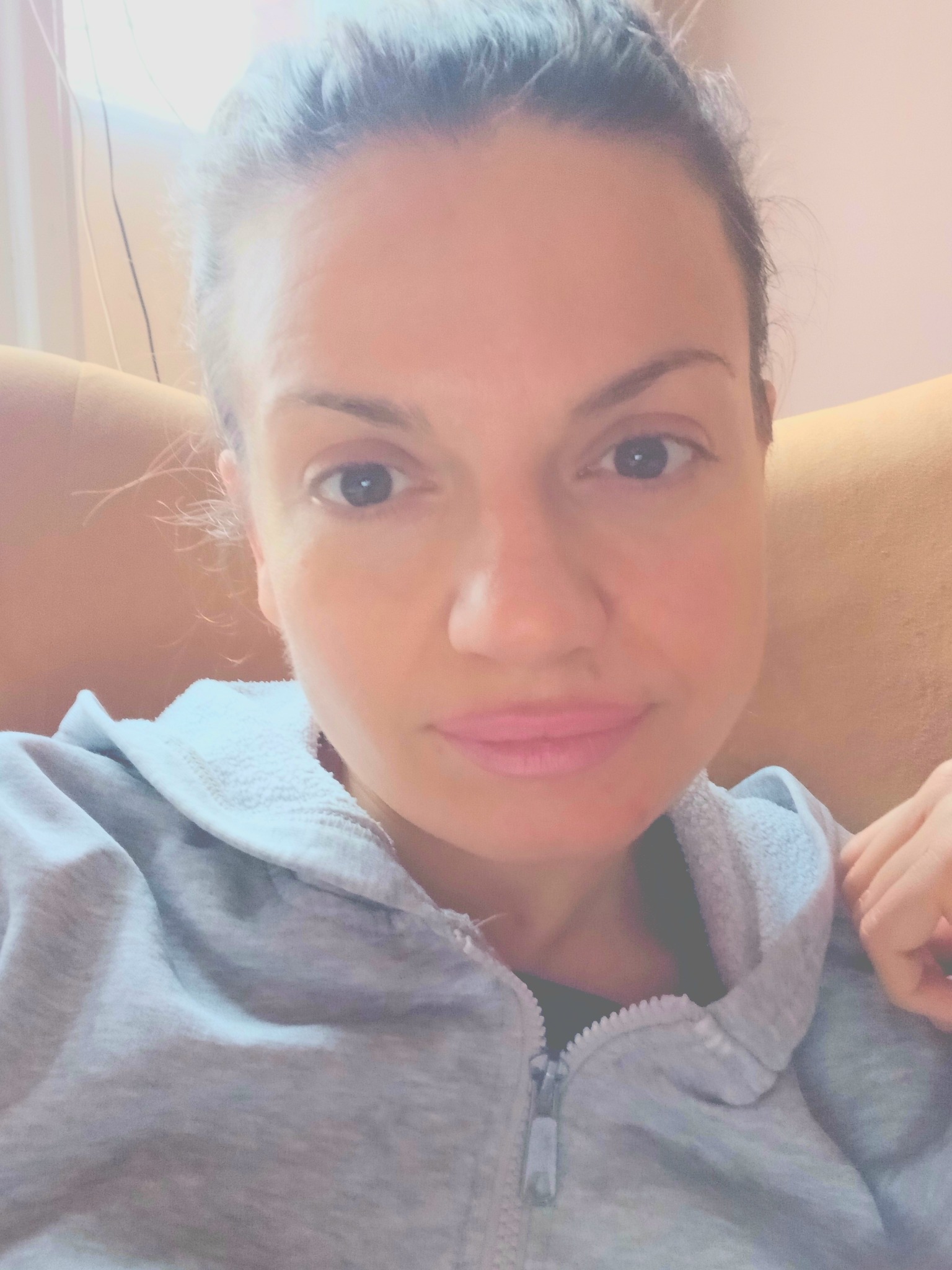 Portret kobiety w szarej bluzie z kapturem, z delikatnym uśmiechem, wykonany w Malborku. Naturalne światło podkreśla rysy twarzy.