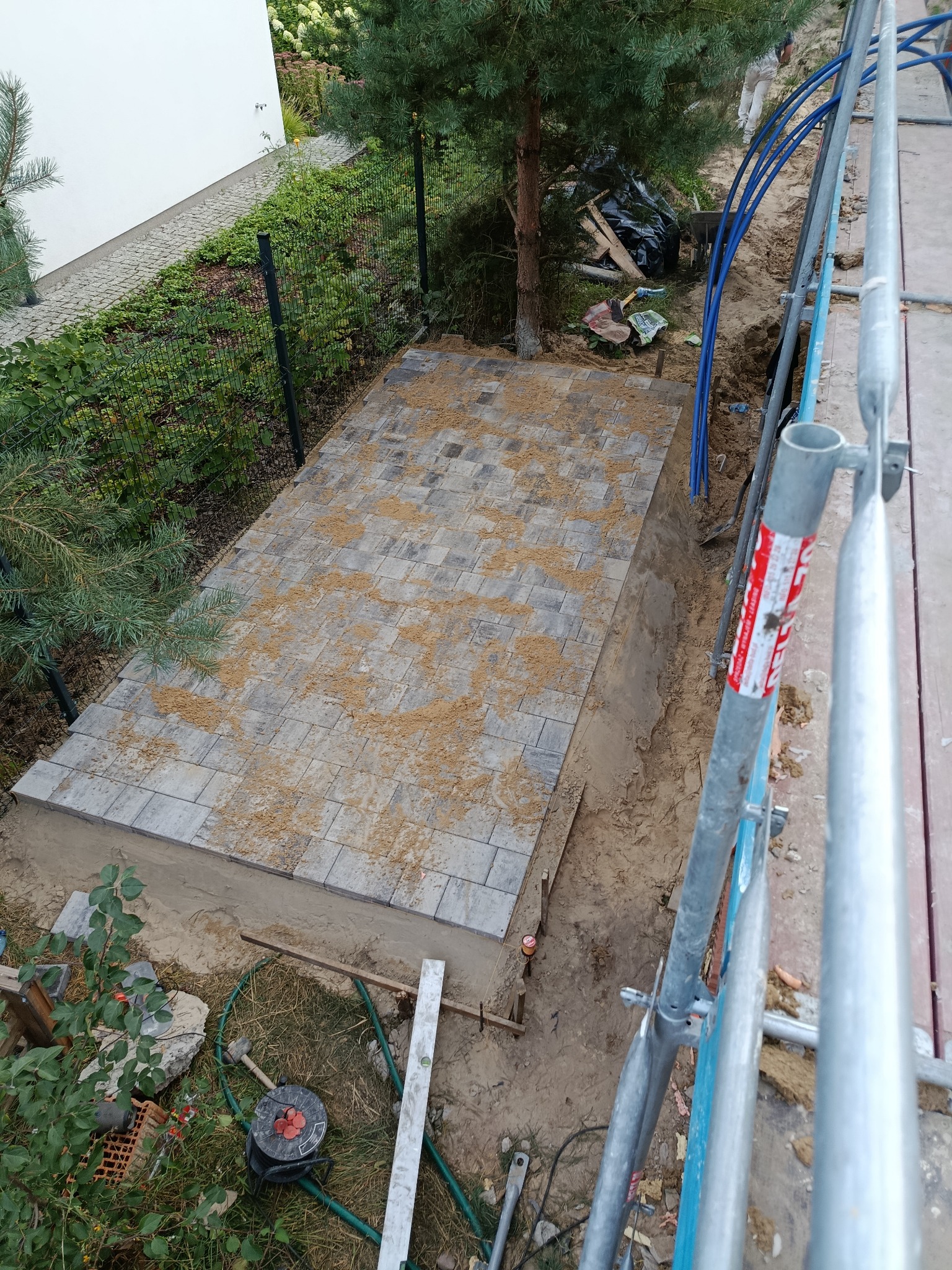 Ułożona kostka brukowa w wykopie, zasypana piaskiem, widok z góry z rusztowania. Przygotowanie podłoża pod taras lub chodnik.