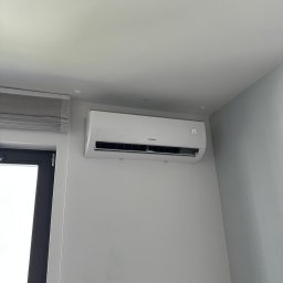 COLDWARM Kacper Rochniak - Biały klimatyzator Kaisai, zamontowany na szarej ścianie w pokoju z roletami. Na wyświetlaczu widoczna temperatura 17 stopni.