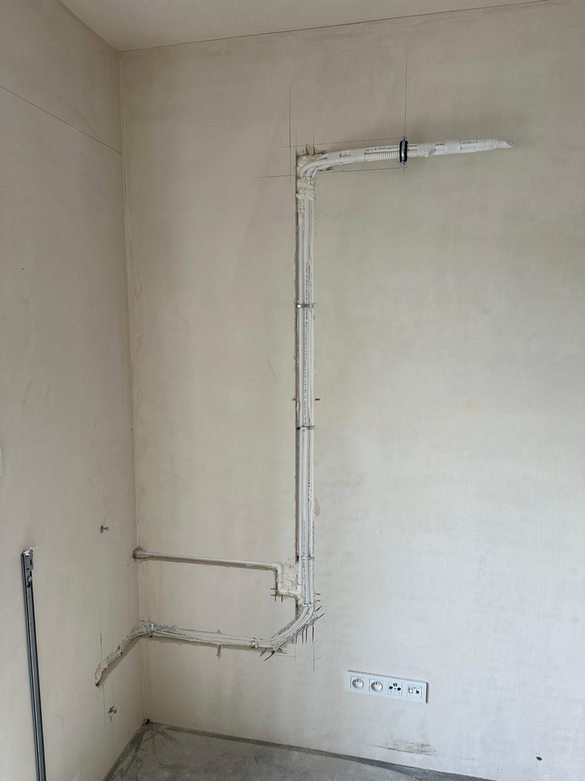 Białe rury wentylacyjne zamontowane na surowej ścianie. Widoczne gniazdka elektryczne. Instalacja w trakcie montażu, zabezpieczona pianką montażową.