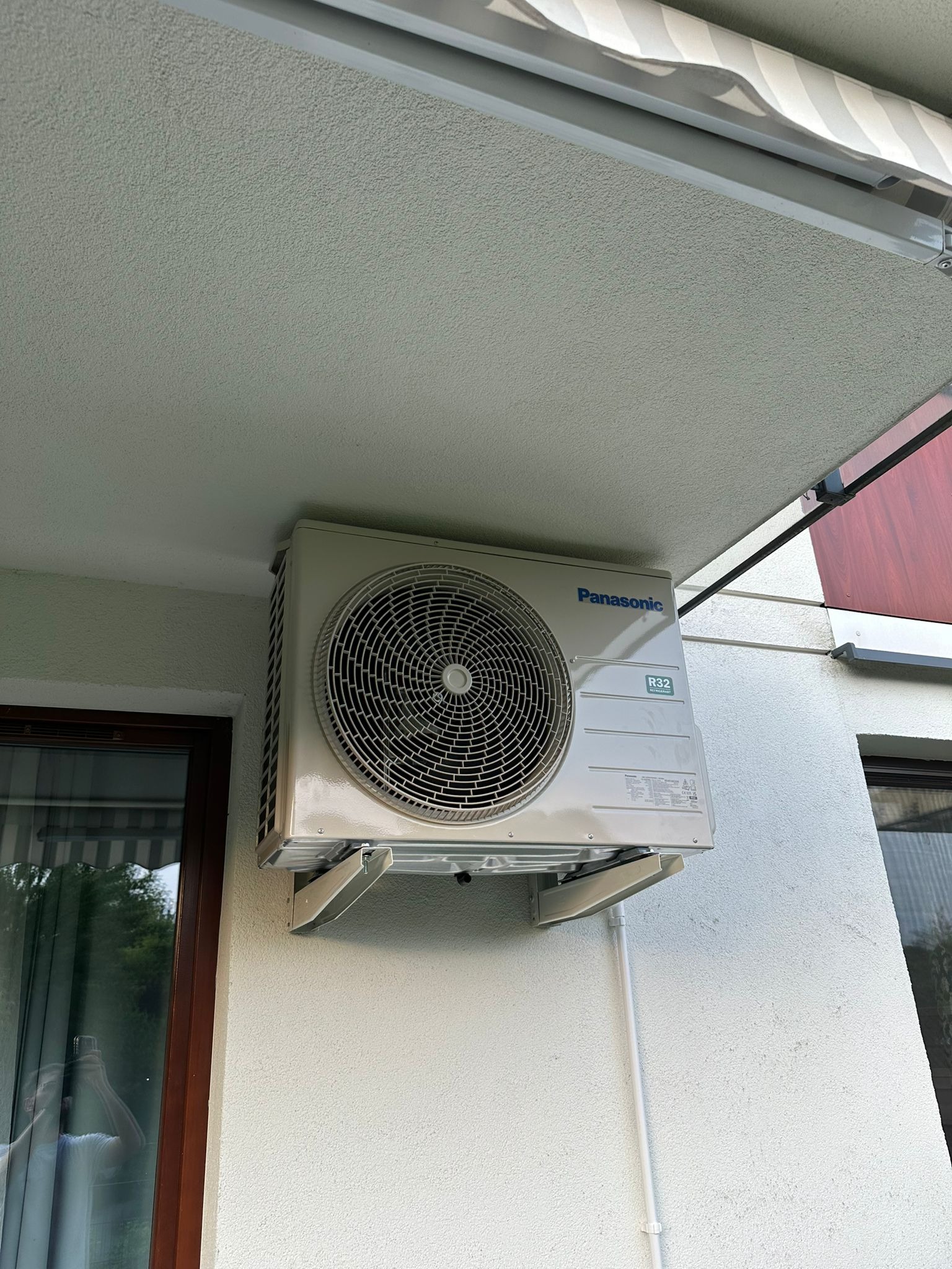 Zamontowana jednostka zewnętrzna klimatyzacji Panasonic R32 na elewacji budynku przy oknie. Widoczna markiza i rura odprowadzająca skropliny.