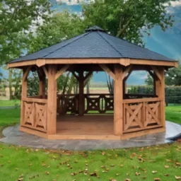 Ośmiokątna, drewniana altana ogrodowa z ciemnym dachem z gontu bitumicznego, otoczona zielenią. Dekoracyjne krzyżowe panele w balustradach.