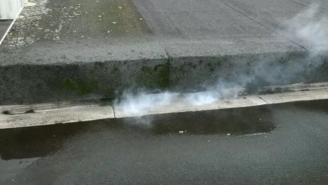 Wyciek dachu z papy bitumicznej, z którego wydobywa się para wodna. Widoczne uszkodzenia i wilgoć. Przeciek zarysowany na szarym tle dachu.