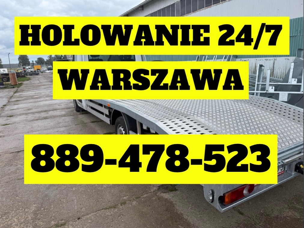 Laweta z żółtymi napisami 'Holowanie 24/7 Warszawa' i numerem telefonu. Widok z boku, na zewnątrz, w tle budynek. Metalowa platforma lawety z bliska.
