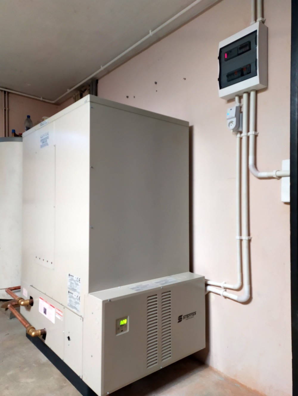 Zamontowana pompa ciepła Steffes w pomieszczeniu technicznym, z widocznymi rurami miedzianymi i skrzynką elektryczną na ścianie.