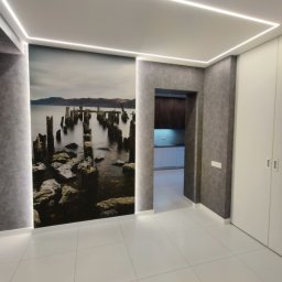 Prof&work Volodymyr Pasichnyk - Nowoczesne wnętrze z fototapetą przedstawiającą krajobraz morski, oświetleniem LED w suficie i białymi płytkami podłogowymi. Widoczne drzwi do innego pomieszczenia.