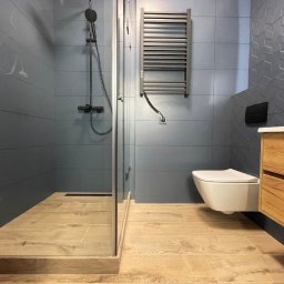 Prof&work Volodymyr Pasichnyk - Nowoczesna łazienka w odcieniach szarości z drewnianymi akcentami. Kabina prysznicowa typu walk-in, podwieszana toaleta i grzejnik drabinkowy.