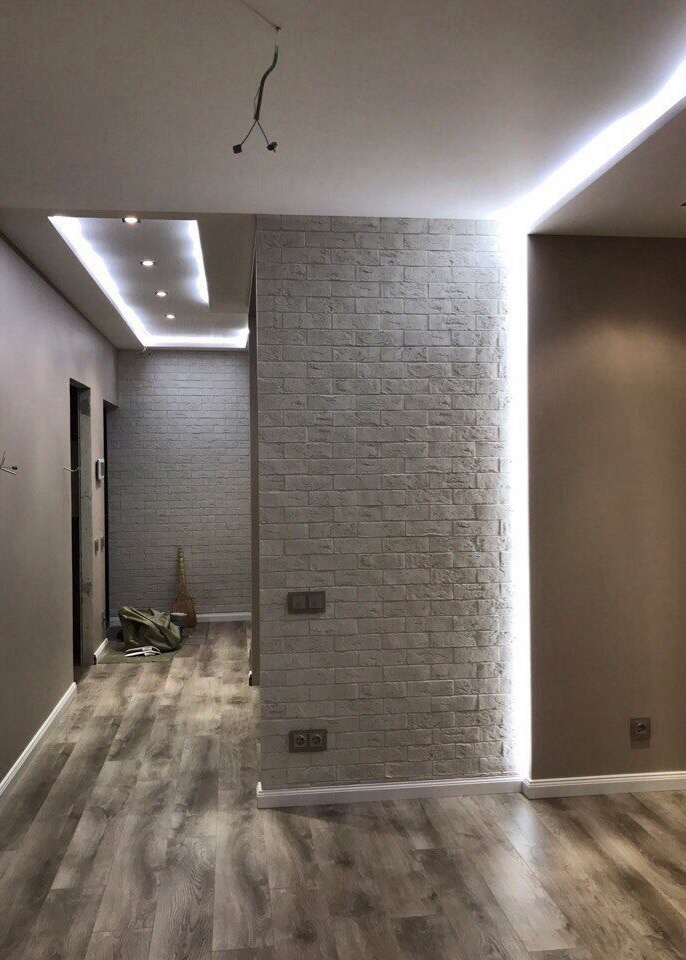 Korytarz po wykończeniu: ściana z cegły dekoracyjnej, podświetlenie LED, drewnopodobna podłoga, widoczne gniazdka elektryczne i elementy instalacji pod sufitem.