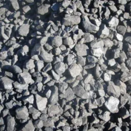 Kupa czarnych bryłek węgla brunatnego o nieregularnych kształtach, oświetlona jasnym światłem słonecznym, ukazująca strukturę materiału.