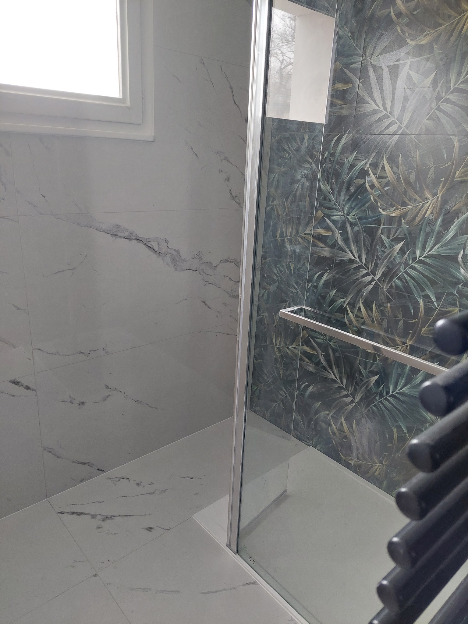 Nowoczesna kabina prysznicowa z marmurowymi i roślinnymi płytkami, chromowany uchwyt, jasne wnętrze, widok z boku, minimalistyczny design.