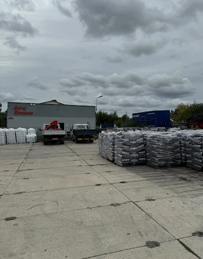 Skład opału z zapasem workowanego węgla i ekogroszku na placu, ciężarówki w tle. Widok na budynek firmy Auto Dragon.