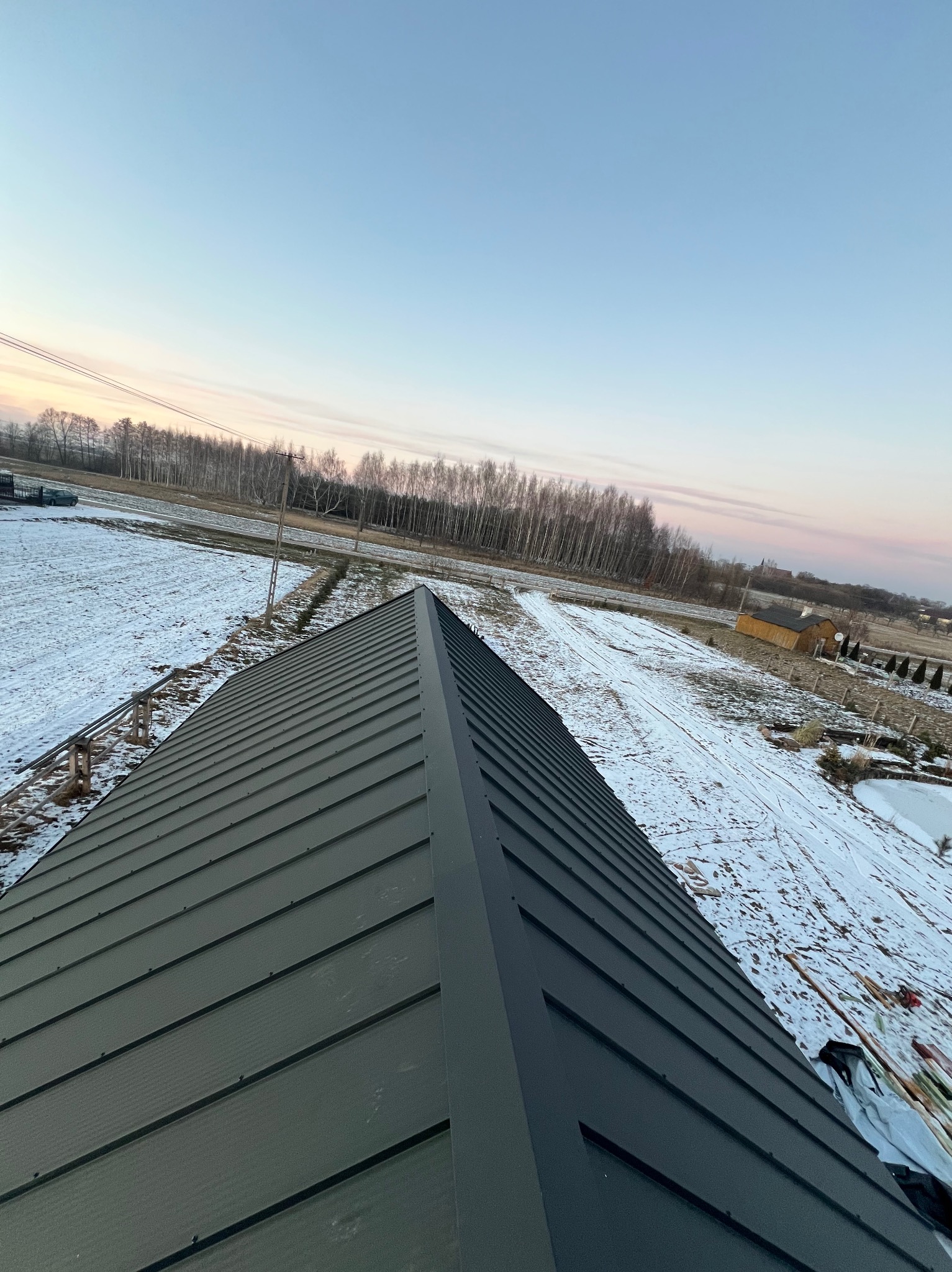 Nowoczesne krycie dachu blachą na rąbek stojący w zimowym krajobrazie. Widok z góry ukazuje precyzję wykonania i estetyczne połączenie z otoczeniem.