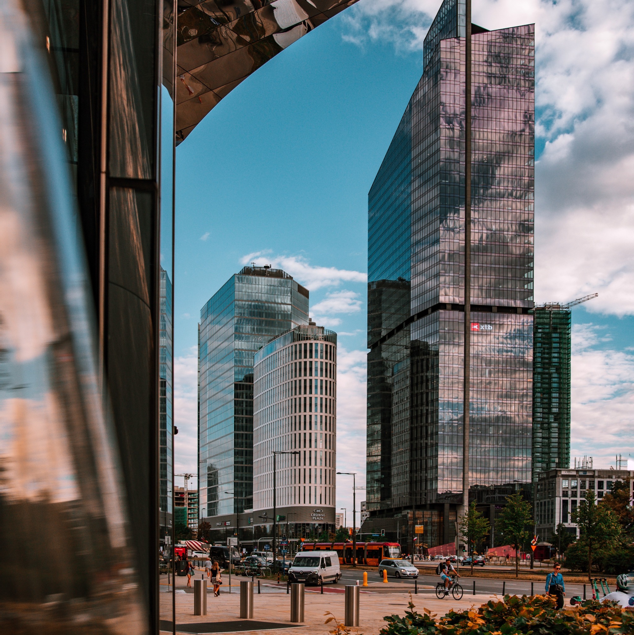 Nowoczesna architektura: szklane wieżowce w centrum miasta, odbijające się w lustrzanej powierzchni budynku. Dynamiczne ujęcie z perspektywy przechodnia.