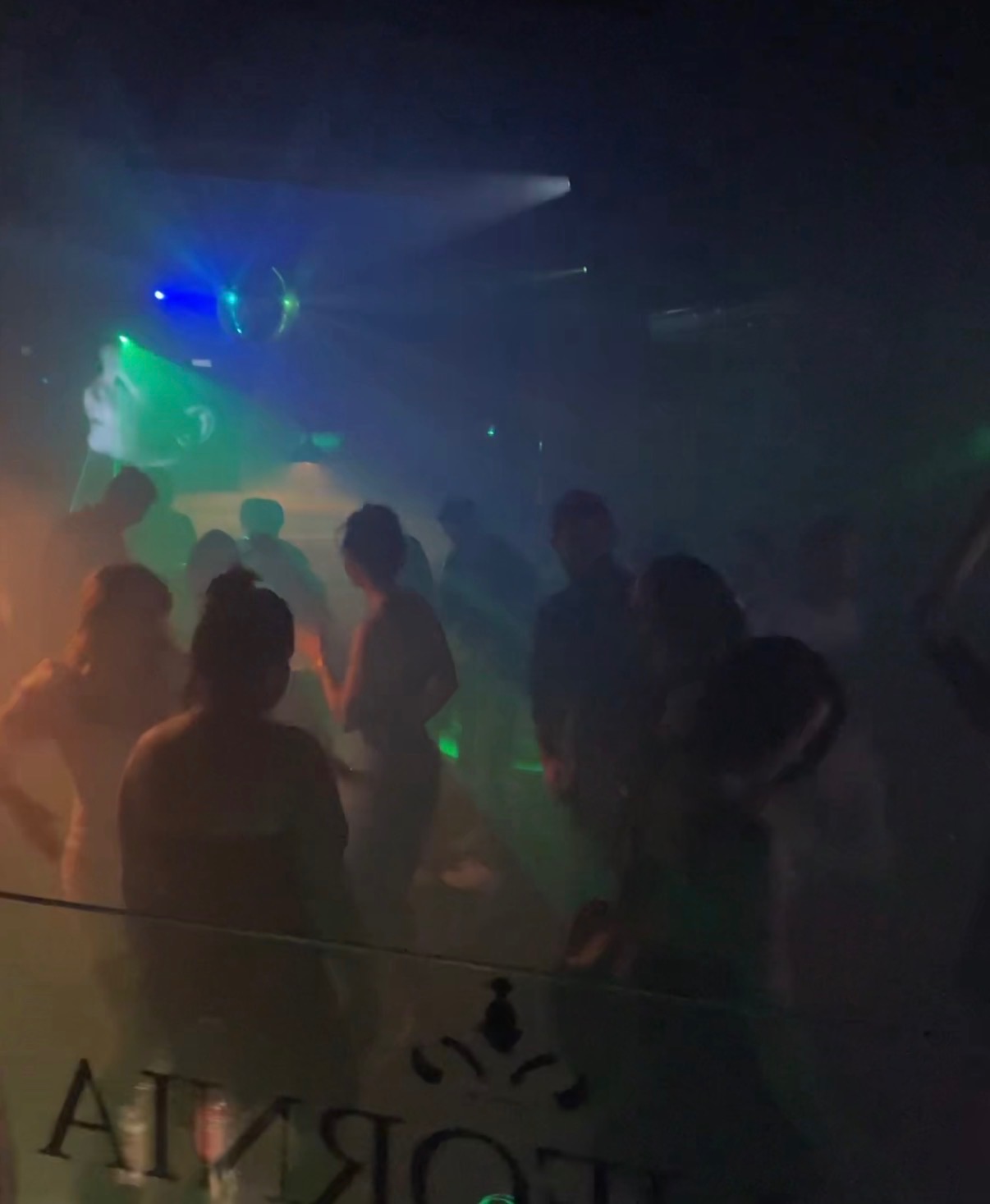 Rozświetlony parkiet taneczny z bawiącymi się ludźmi w dyskotekowym klimacie, oświetlony kolorowymi światłami i dyskotekową kulą.