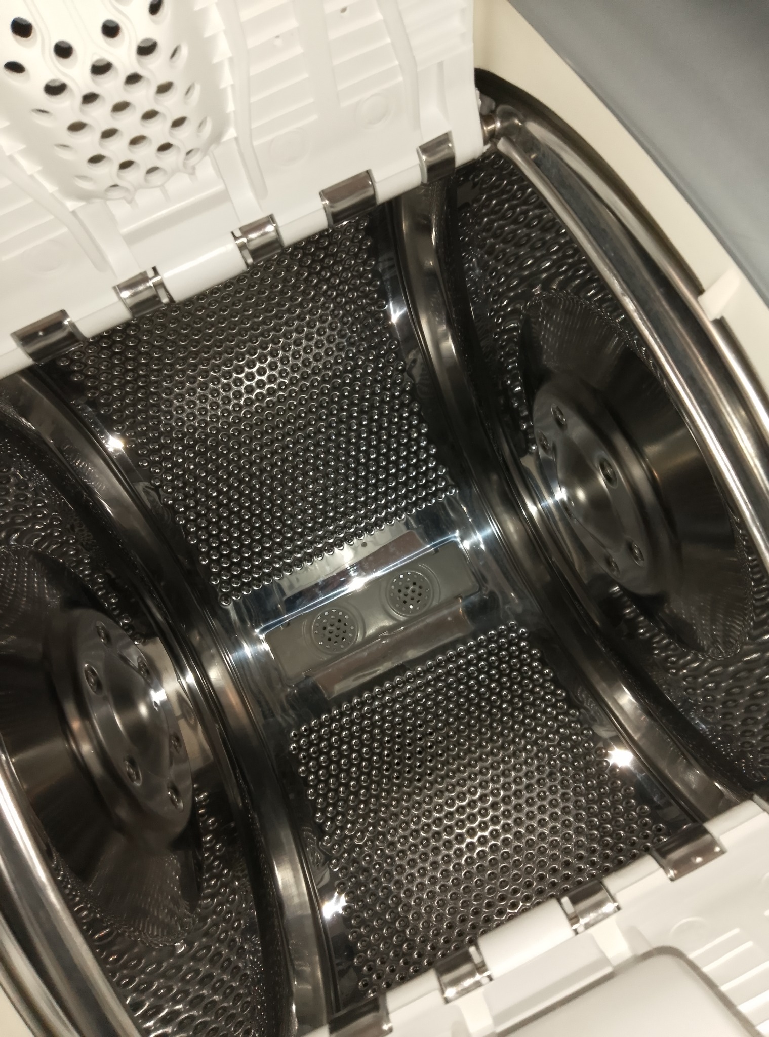 Wnętrze bębna pralki automatycznej z widocznymi otworami i elementami mocującymi, uchwycone z góry pod kątem, ukazujące detale konstrukcyjne.