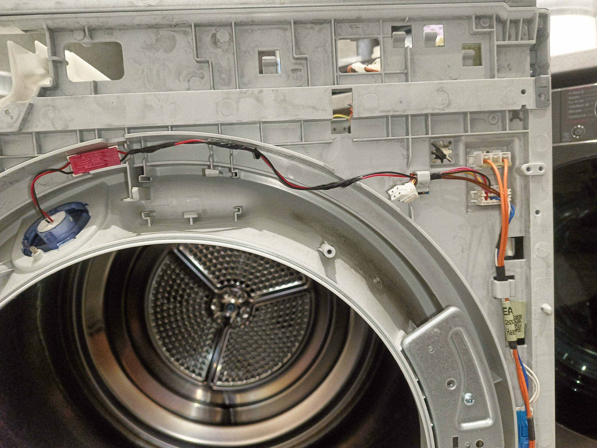 Wnętrze pralki automatycznej w trakcie naprawy: widoczne przewody, bęben i elementy konstrukcyjne. Detal z bliska, ukazujący specyfikę serwisu AGD.