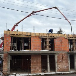 T&O Company - Wylewanie betonu na strop budynku w trakcie budowy. Widoczny żuraw do betonu, pracownicy w kaskach i surowy stan budynku z czerwonej cegły.