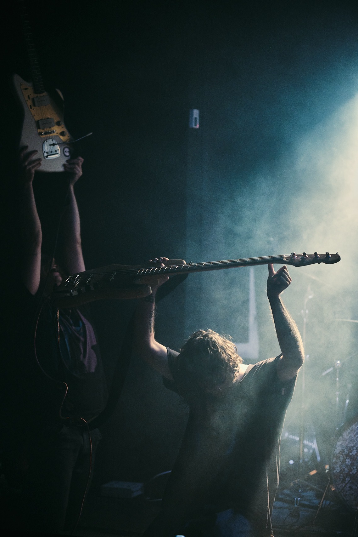 Ekstatyczny tłum unosi gitary podczas koncertu w zadymionym klubie. Zauważalna atmosfera energii i pasji, podkreślona przez punktowe oświetlenie.