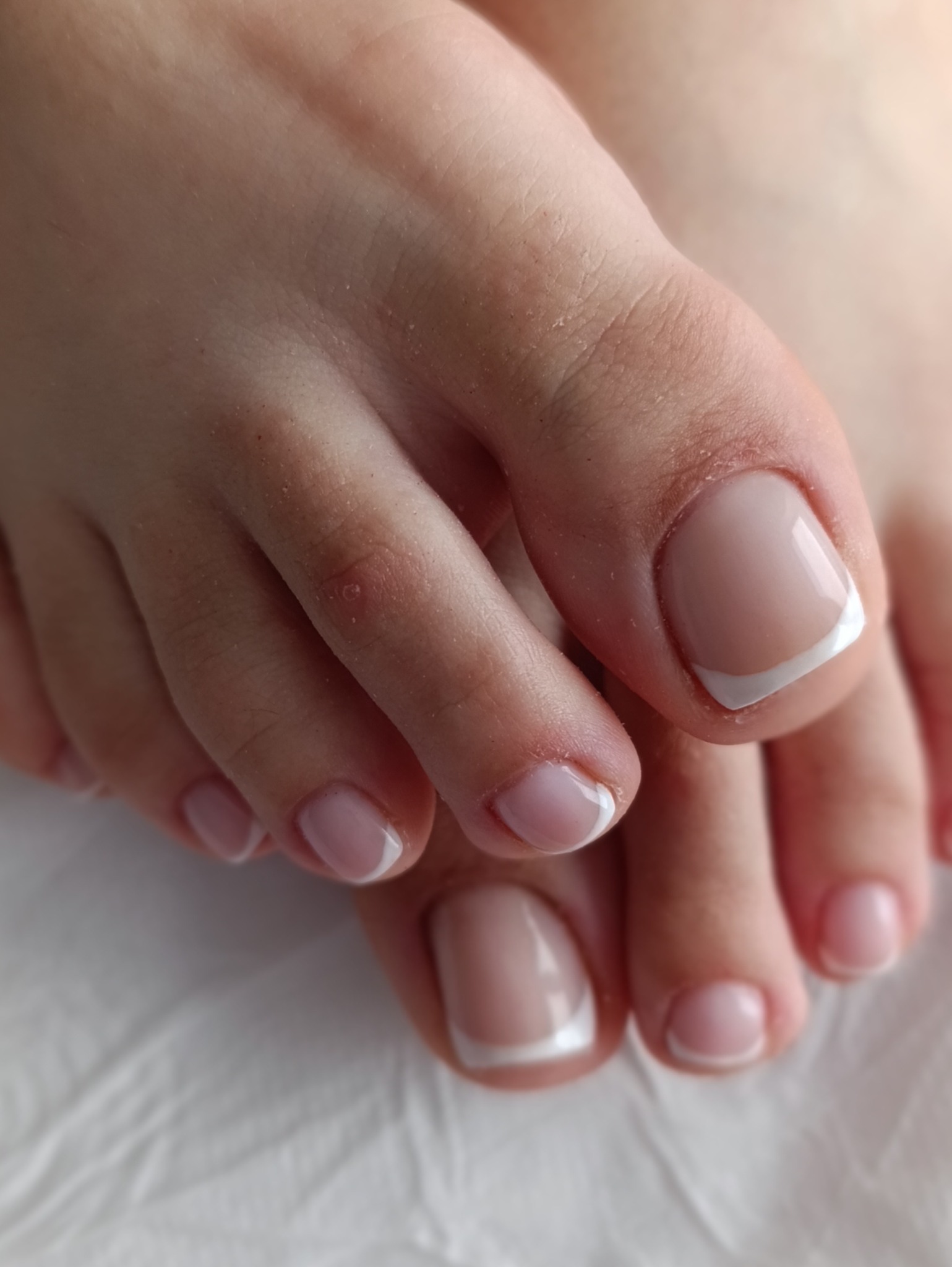 Zbliżenie na stopy z precyzyjnym, klasycznym pedicure francuskim na białym tle. Widoczne detale wykonania i estetyczne wykończenie.