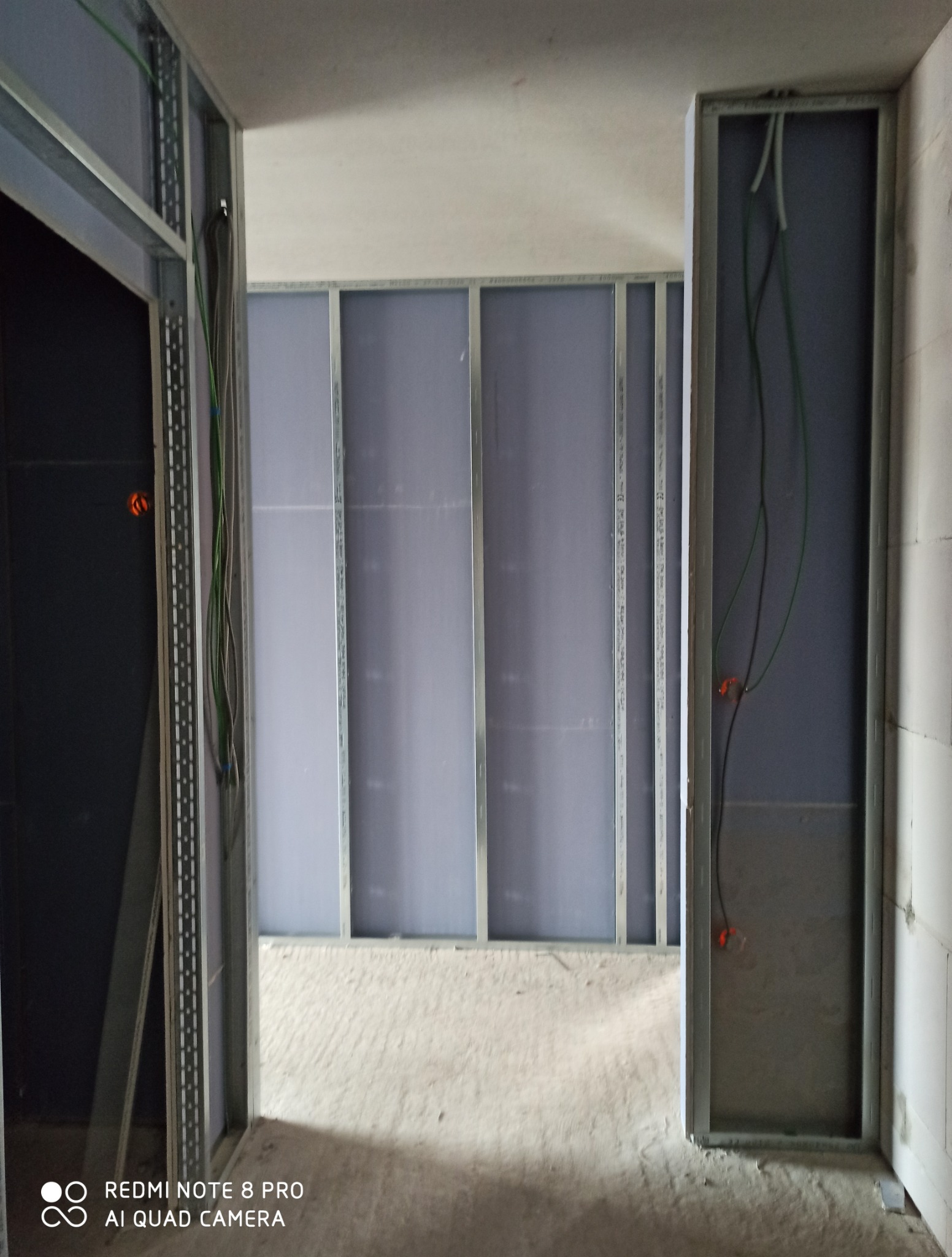 Wnętrze w trakcie montażu ścian działowych z płyt kartonowo-gipsowych na metalowym stelażu. Widoczne kable elektryczne w ścianie. Surowy stan wykończenia.
