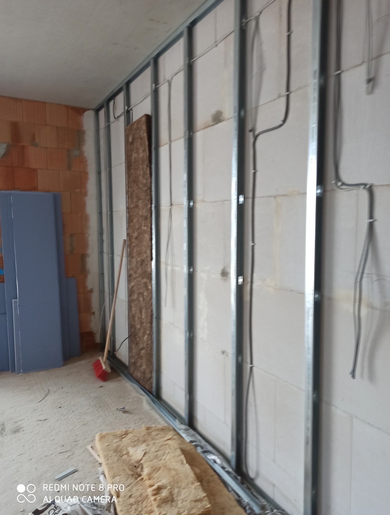 Montaż stelaża pod płytę G-K z widoczną instalacją elektryczną i częściowo ułożoną izolacją. Fragment ściany z cegły i płyty G-K w tle. Prace wykończeniowe.