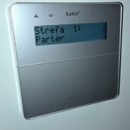 Panel alarmowy Satel Integra z wyświetlaczem LCD, prezentujący status strefy 'Parter'. Srebrna obudowa, widoczne ikony i przyciski funkcyjne.