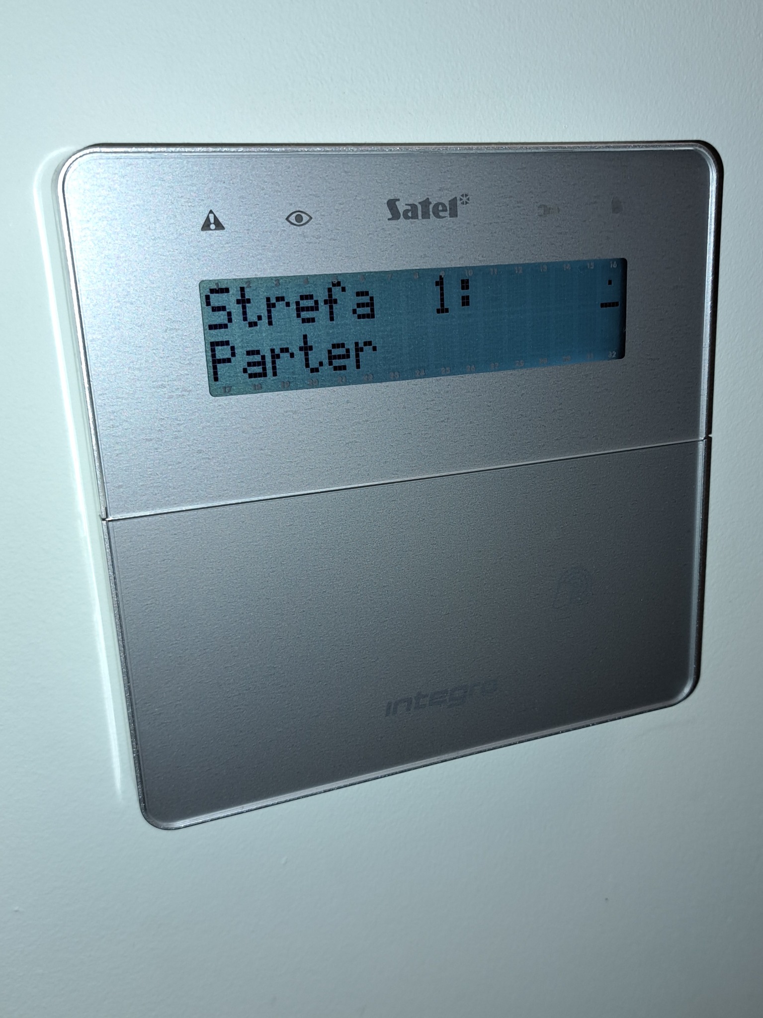 Panel alarmowy Satel Integra z wyświetlaczem LCD, prezentujący status strefy 'Parter'. Srebrna obudowa, widoczne ikony i przyciski funkcyjne.