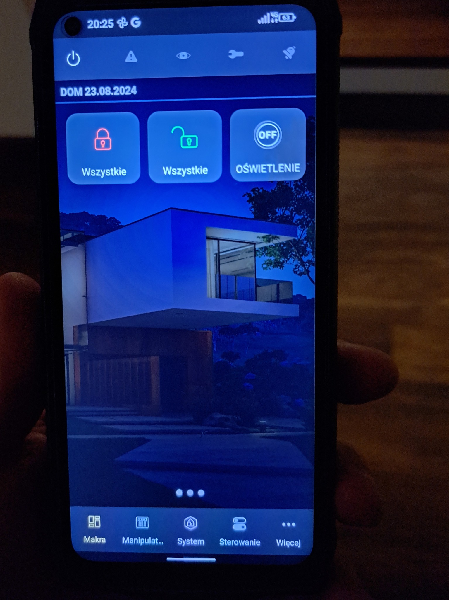 Ekran smartfona z aplikacją do zarządzania inteligentnym domem: kontrola oświetlenia, alarmu i dostępu. Widok domu z włączonym oświetleniem w tle aplikacji.