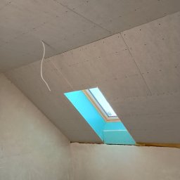 Piotr Najdowski - Poddasze w trakcie wykańczania: zamontowane płyty karton-gips na skosach, widoczne okno dachowe i wystający kabel. Ściany częściowo wyszpachlowane.