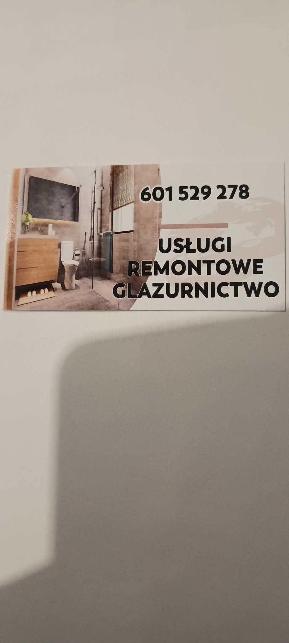 Wizytówka firmy z numerem telefonu i napisem 'Usługi remontowe, glazurnictwo'. Na wizytówce zdjęcie łazienki z drewnianą szafką, toaletą i kabiną prysznicową.