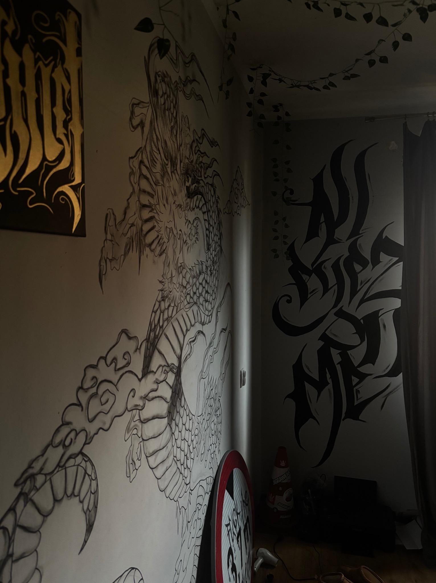 Pokój z muralami: czarny smok i abstrakcyjne wzory na ścianach, dekoracje roślinne na suficie. Nietypowe oświetlenie i styl artystyczny tworzą unikalny klimat wnętrza.