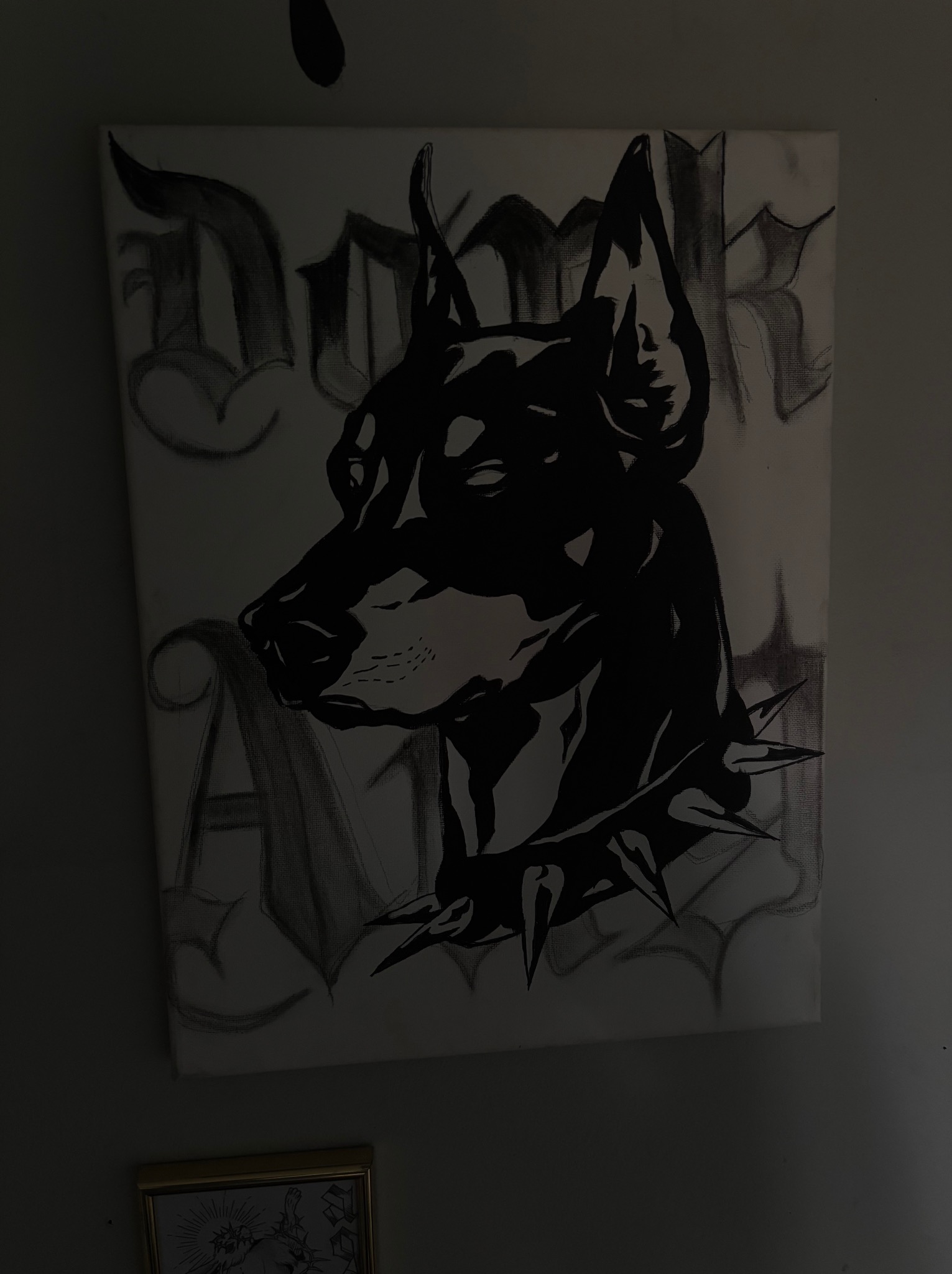 Ręcznie malowany obraz na płótnie: portret dobermana w kolczatce, w stylu graffiti, czarno-biały. Ujęcie z bliska, widoczny fragment ramy obrazu.